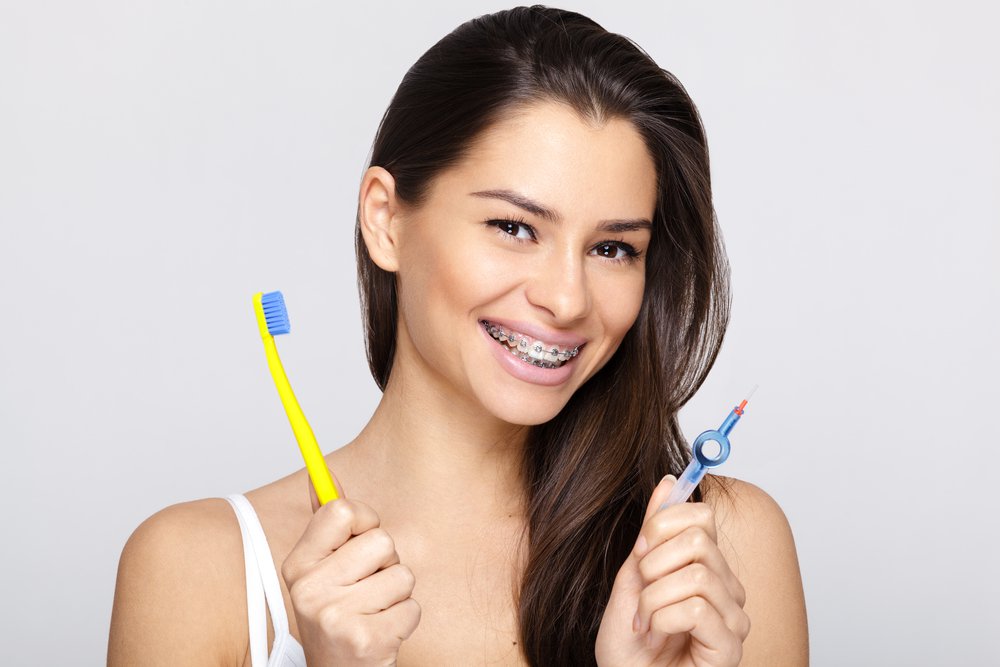 a woman smiles wearing braces while she holds up dental cleaning tools